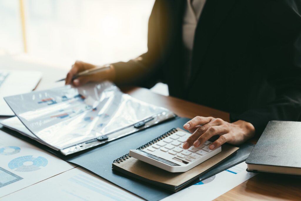 Person using calculator and holding a pencil looking at a binder of documents